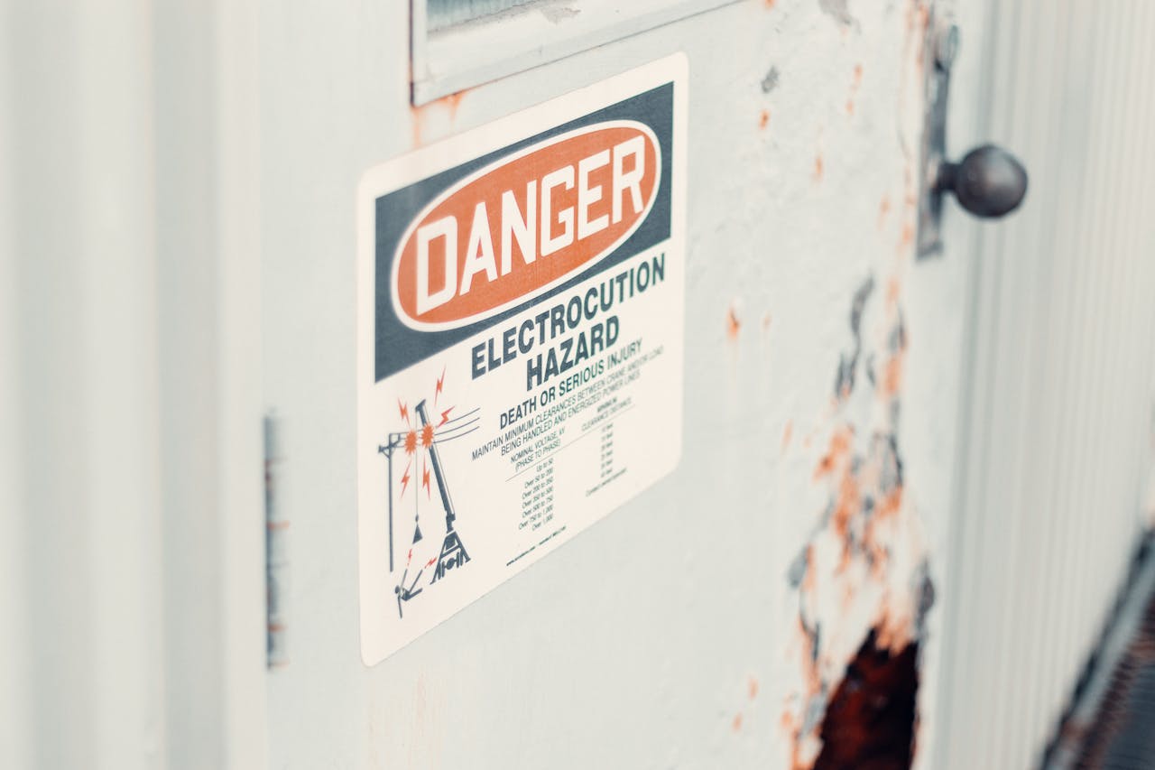 Close-up of a danger sign warning of electrocution hazard on a rusty utility door, indicating safety precautions.